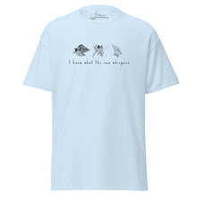 Load image into Gallery viewer, Light blue t-shirt featuring minimalist line drawings of clams (achivades) and sea snails, with the phrase 'I know what the sea whispers' printed on the front.